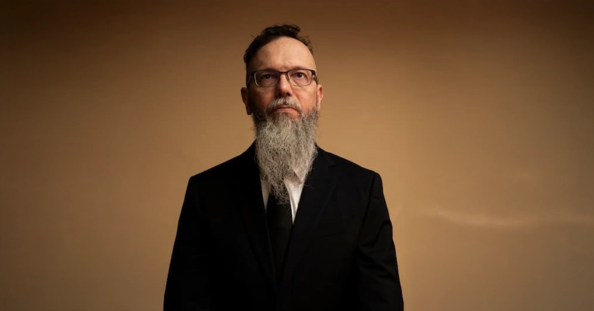 Eric Bravick standing in a suit against a warm background